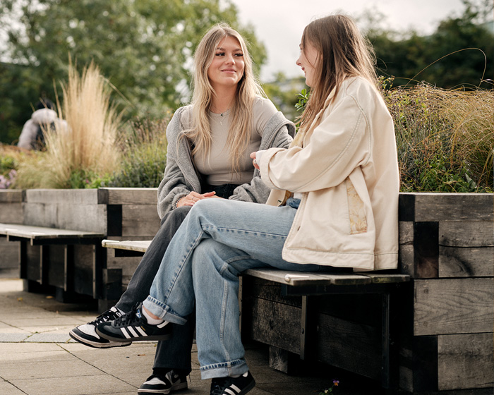 Two female students sat on a bench talking